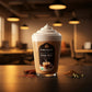 Tall glass of Pure Bliss Chai Milk topped with whipped cream, surrounded by cinnamon and cardamom spices in a cafe setting